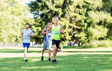 fitness, sport, race and healthy lifestyle concept - group of happy people or male sportsmen running marathon with badge numbers at summer park