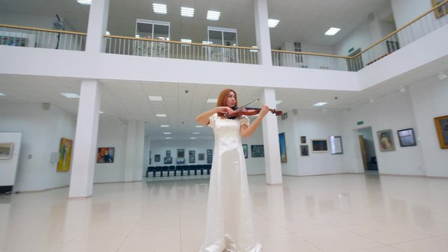 Gorgeous woman is playing the violin in a museum