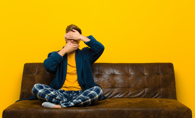 young man wearing pajamas covering face with both hands saying no to the camera! refusing pictures...