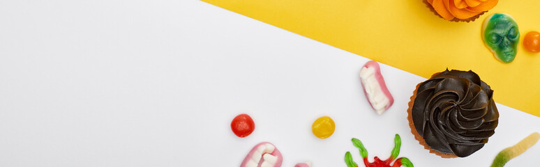 panoramic shot of colorful gummy sweets and cupcakes on yellow and white background, Halloween treat