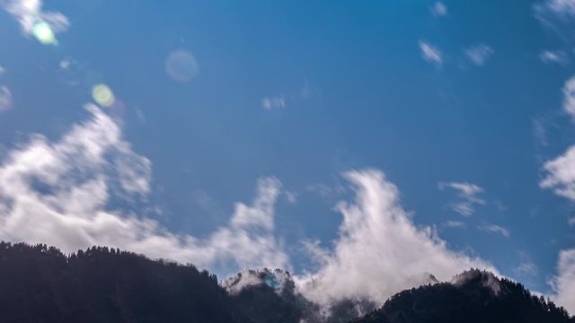 Fast-moving clouds gradually cover the blue sky over a mountain range