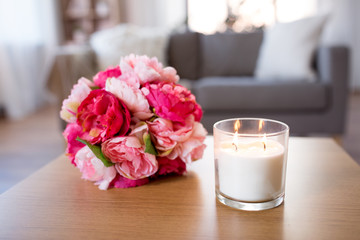decoration, hygge and cosiness concept - burning fragrance candle and flower bunch at cozy home
