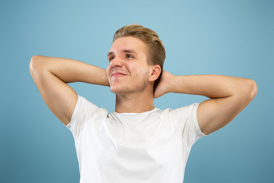 Caucasian young man's half-length portrait on blue studio background. Beautiful male model in shirt. Concept of human emotions, facial expression, sales, ad. Resting and chilling, smiling. Copyspace.