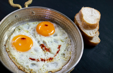 two eggs cooked in a copper pan and sliced bread beside