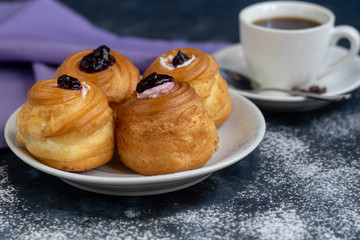 Fragrant, hot coffee. On a plate are cupcakes with cream filling. Everything is located on a dark background. 