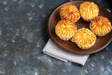 On a brown clay plate are cupcakes with cream filling. In the background is a gray, cloth napkin. Everything is located on a dark background