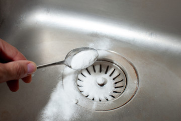 Baking soda in a spoon over a dirty dishwasher sink