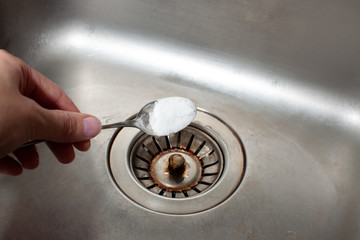 Baking soda in a spoon over a dirty dishwasher sink