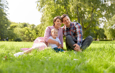 Naklejka na ściany i meble family, leisure and people concept - happy mother, father and little son at summer park sitting on grass