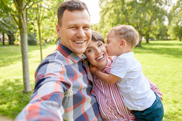 family, leisure and people concept - happy mother, father and little son taking selfie at summer park