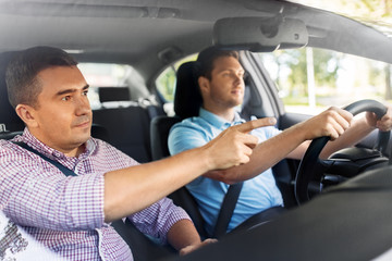 driver courses and people concept - car driving school instructor teaching young man to drive