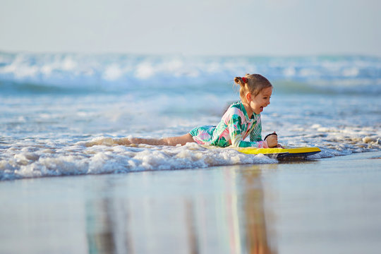 foamy waves of the beautiful autumn sea splashing alongside a charming little girl on a yellow surfboard