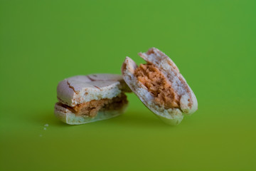 One broken macaron tastefully salted caramel on one-ton green background. French dessert. Sweets.