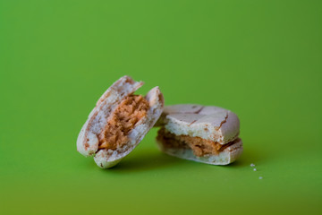 Fototapeta na wymiar One broken macaron tastefully salted caramel on one-ton green background. French dessert. Sweets.
