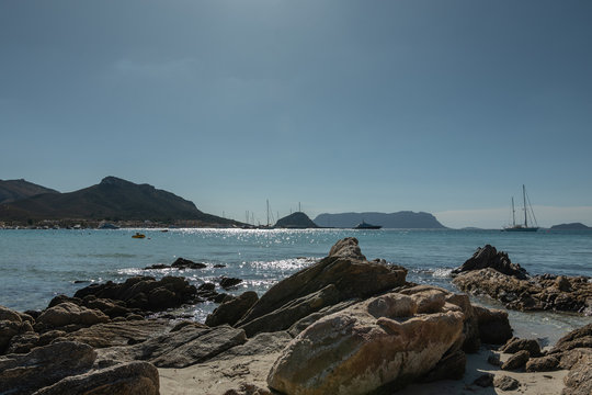 View from the rocks on the shore of the sea with yachts on the background of mountains and blue sky