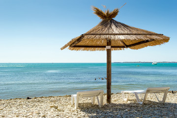 Vacation background. Two deckchairs and umbrella on a beach. Blue water of sea bay. Pebbles under your feet.