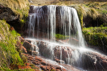 Obraz premium Cascades of powerful Monk's jump waterfall, the tallest in Serbia, streaming down the wet, red cliff rocks during early spring