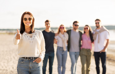 Obraz premium friendship, leisure and people concept - happy woman in sunglasses with group of friends on beach in summer showing thumbs up