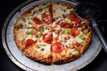 Whole sliced hot pizza on round pizza pan with pizza cutter on dark background