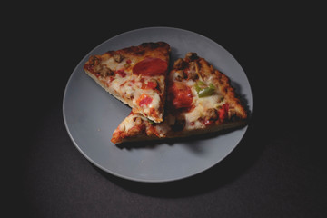 Two slices of hot pizza on blue-gray saucer with dark background