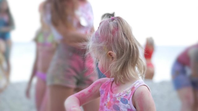 A cute little girl participates in a paint festival by playing with colorful paints and sand. His face and clothes were stained with bright colors.