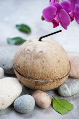 Close-up of a natural coconut drink, vertical shot on a beige stone surface with pebbles