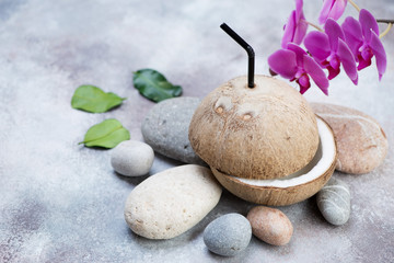 Fototapeta na wymiar Natural coconut drink on a beige stone background with pebble stones and orchid, horizontal shot with copyspace