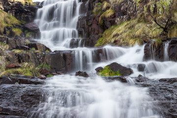 Low perspective, long exposure, close up composition of scenic Monk's jump waterfall on Old mountain, cascading down the sunlit dark red rocks