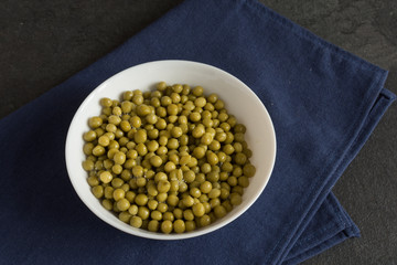White bowl with canned green peas.