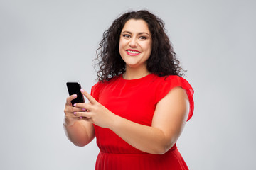 Naklejka premium technology, people and communication concept - happy woman in red dress using smartphone over grey background