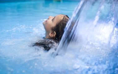 7 years little girl enjoying waterfall jets at indoor pool SPA