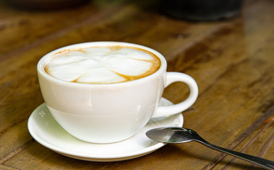 Beautiful flower latte art in white coffee cup and silver teaspoon isolated on wooden table in coffee shop.
