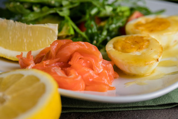 Salad with salted trout, avocado, arugula and fried egg in butter. Close up on the grey background