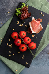Prosciutto, cherry tomatoes and pine nuts. Fresh appetizer on the black board