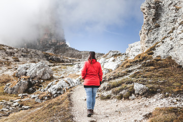 Fototapeta premium Female hiker with red jacket on a hike ontop a peak of tres cimes mountain in south tyrol. Motivational and inspirational scene. Cloudy and very contrasty dramatic edit.