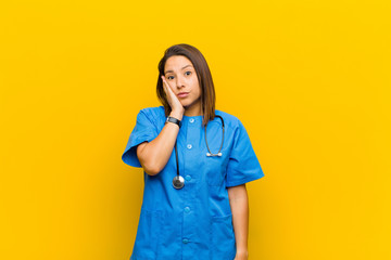 feeling shocked and astonished holding face to hand in disbelief with mouth wide open isolated against yellow wall