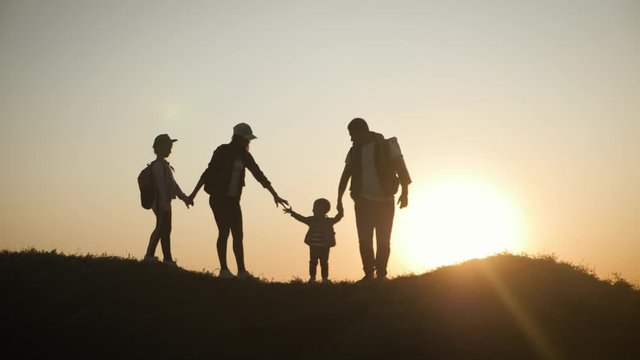Parents and two children walking in the mountains at the sunset time. Silhouette happy beautiful family during the travelling. Concept of friendly family and travel.