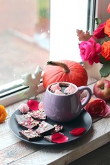 Cup of coffee, chocolate with spices, meringues, roses, pumpkins, leaves on a wooden surface on a window background, home comfort concept, Thanksgiving, autumn season