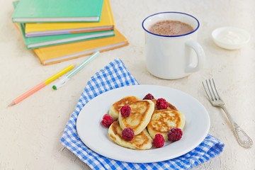 Breakfast, pancakes with sour cream and raspberries on a white plate on a light concrete background. Child's breakfast in front of the school. School breakfast concept.