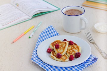 Breakfast, pancakes with sour cream and raspberries on a white plate on a light concrete background. Child's breakfast in front of the school. School breakfast concept.