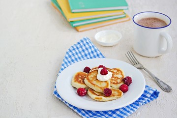 Breakfast, pancakes with sour cream and raspberries on a white plate on a light concrete background. Child's breakfast in front of the school. School breakfast concept.