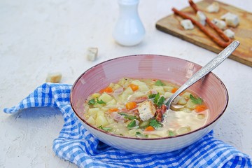 Yellow pea soup with potatoes, carrots, ham and smoked sausages in a clay bowl on a light concrete background. Served with white bread croutons.
