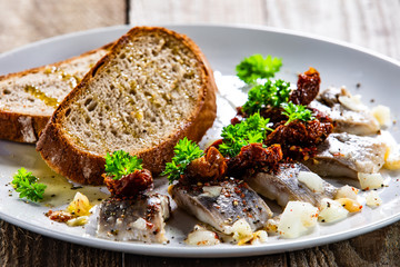 Marinated herring fillets with slices of bread on white plate on wooden table