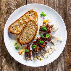Marinated herring fillets with slices of bread on white plate on wooden table