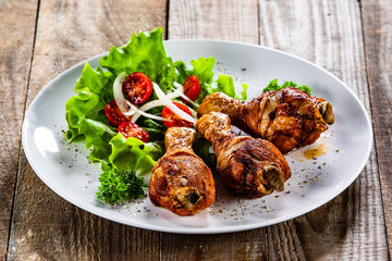 Grilled chicken drumsticks and vegetables on white plate