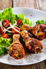 Grilled chicken drumsticks and vegetables on white plate