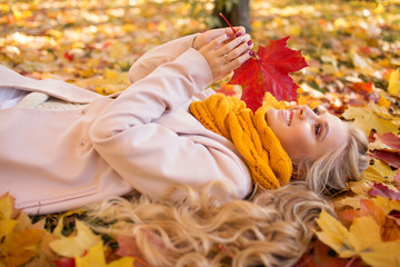 Portrait of pretty blonde teen girl lying on the carpet of yellow leaves