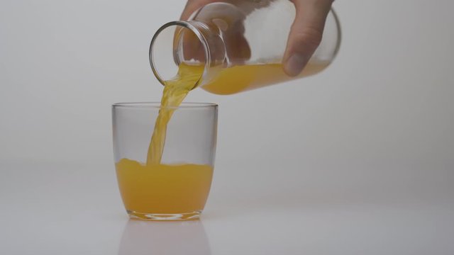 Sweet sugary orange beverage pouring into the glass from the pot. High caloric content drinks. Unhealthy food concept