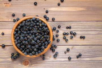 Ripe black currants in a wooden bowl on a wooden table. Top view