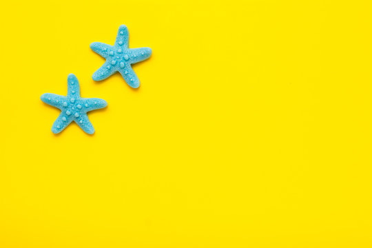 Two blue plastic starfishes on a yellow background. Top view. Place for text